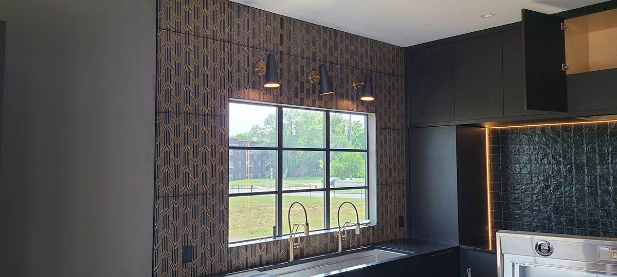 Kitchen with textured wood wall, window with gold faucets, and black cabinets
