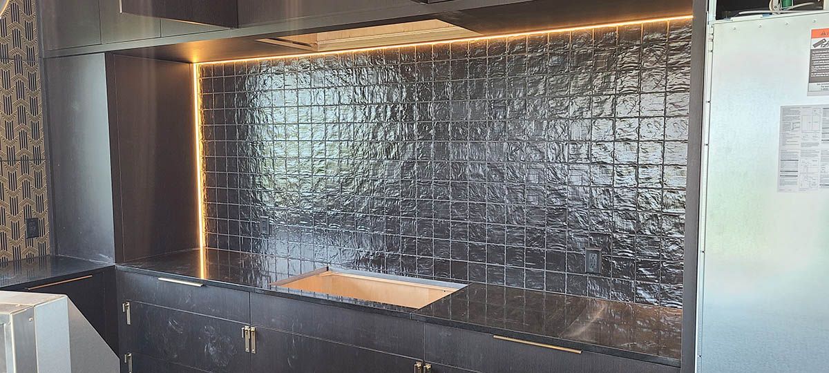 Dark kitchen with black tile backsplash, under-cabinet lighting, and black cabinets