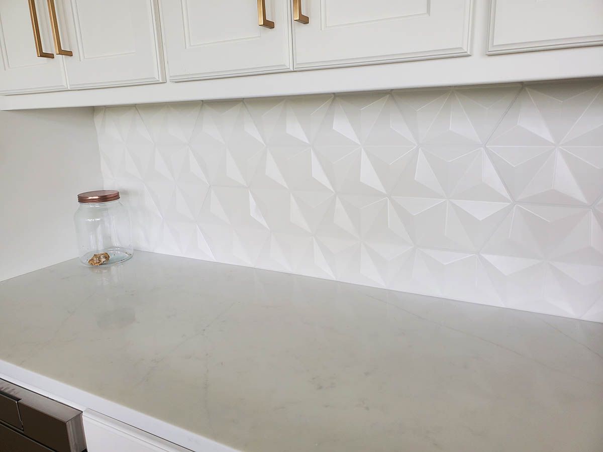 White textured backsplash above a light gray countertop, with white cabinets and gold hardware