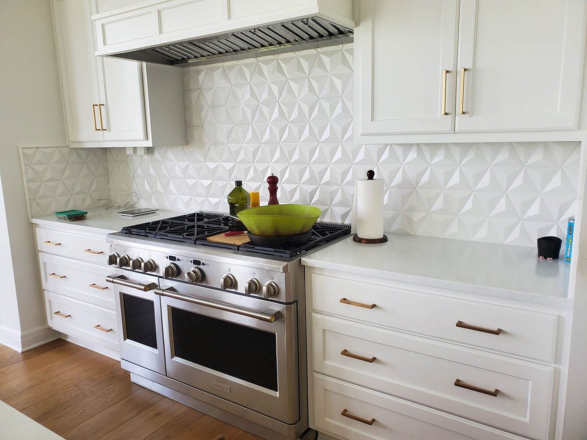 White kitchen with stainless steel stove, geometric tile backsplash, and white cabinets