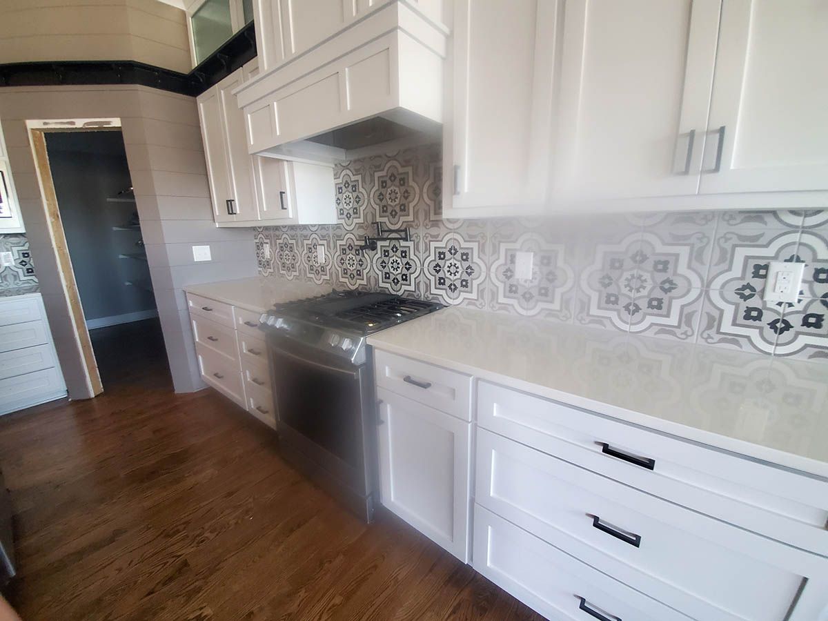White kitchen with patterned backsplash, stainless steel appliances, and dark wood floors