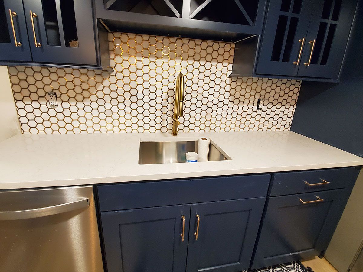 Navy blue cabinets, white countertop, gold fixtures, and hexagon tile backsplash in a kitchen