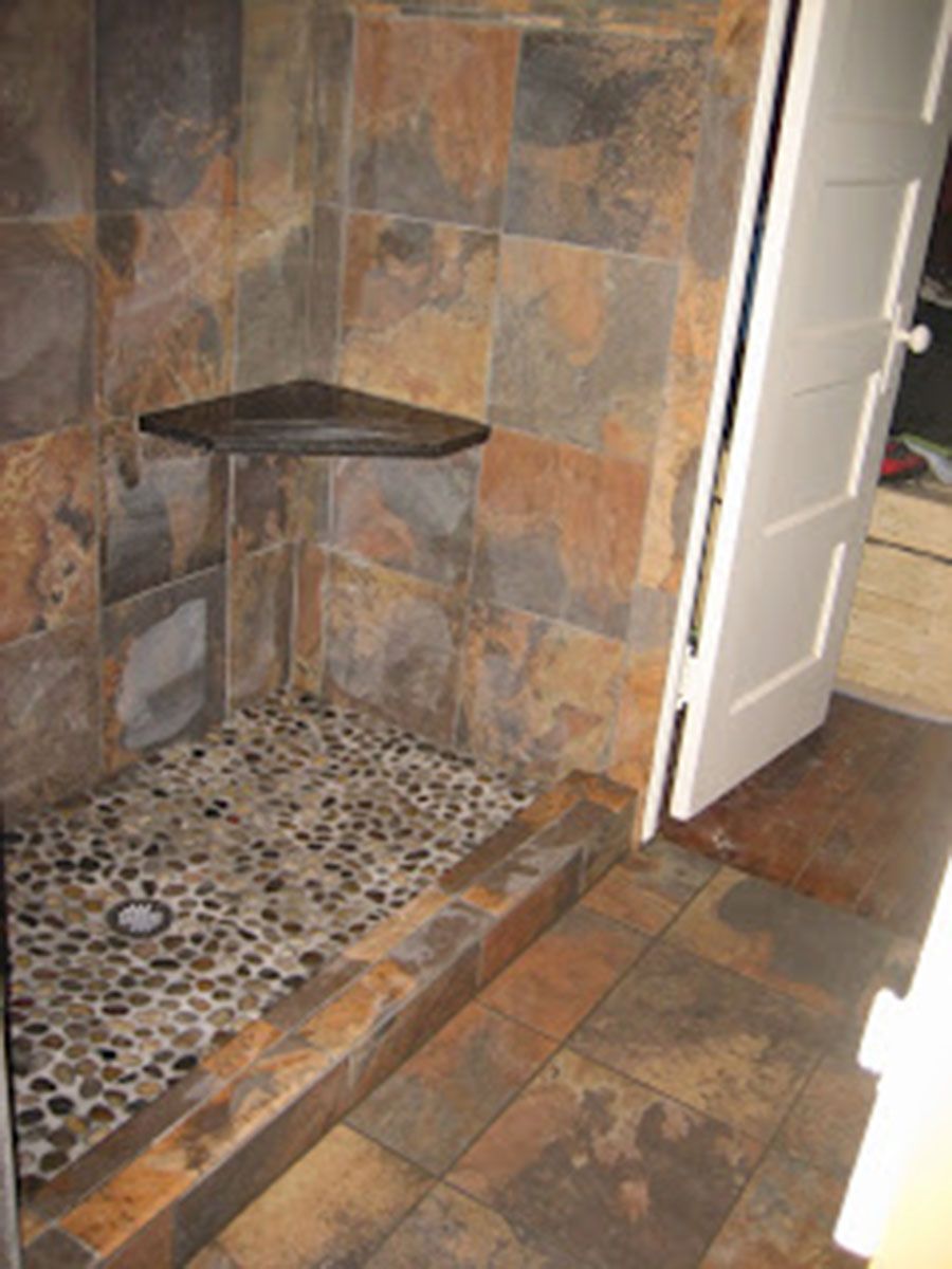 Shower with slate tile walls, pebble floor, and corner shelf; next to an open door