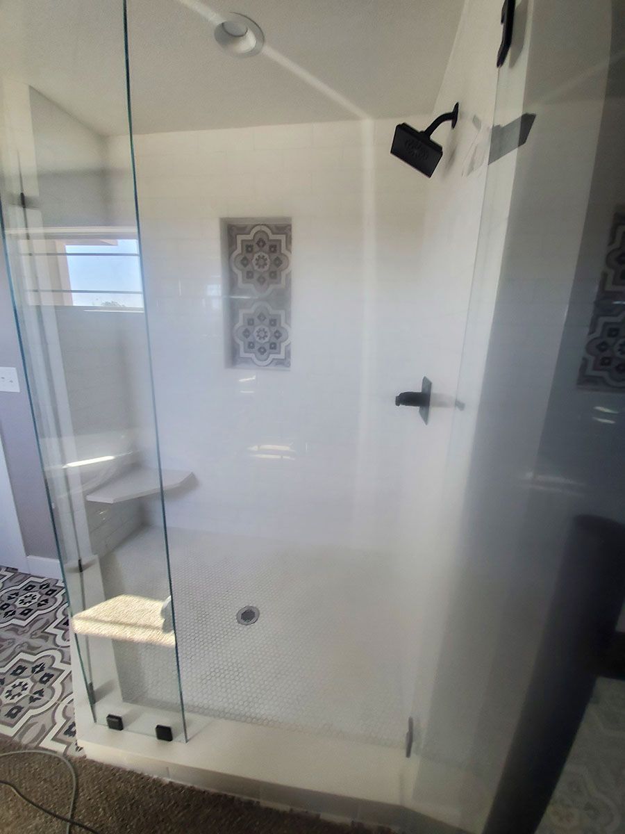 Glass-walled shower with white tile and decorative tile accents. Includes a built-in seat and black shower fixtures