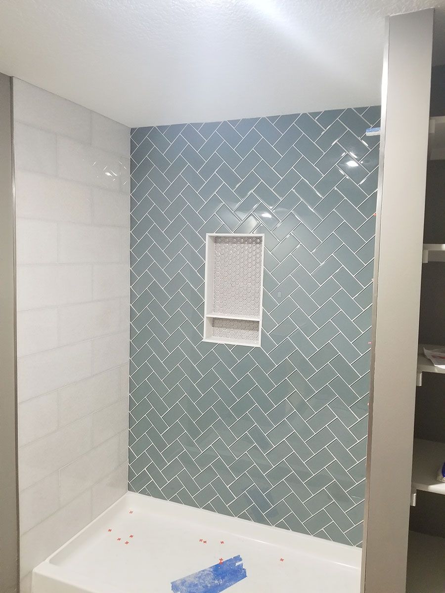 Blue herringbone tile shower wall with built-in niche, white shower base, and white tile side wall