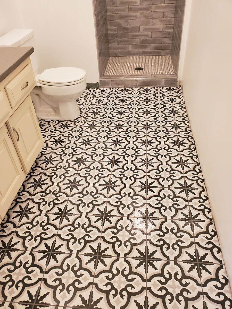Bathroom with black, gray, and white patterned floor tiles, white toilet, and gray tiled shower