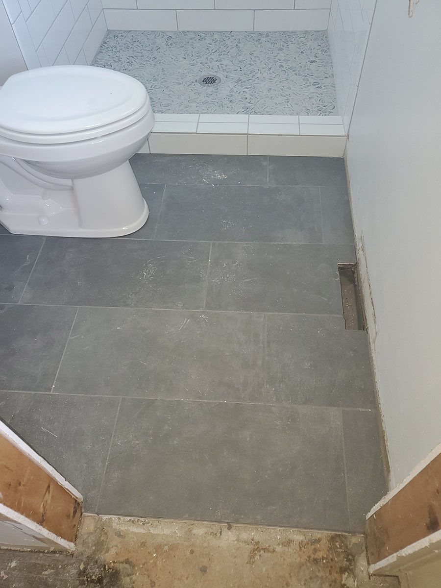 Bathroom with gray tiled floor, a white toilet, and a shower with gray pebbled floor