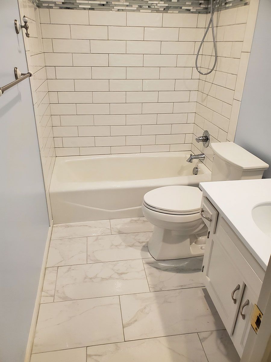 Bathroom with white subway tile shower, white toilet, vanity, and marble floor