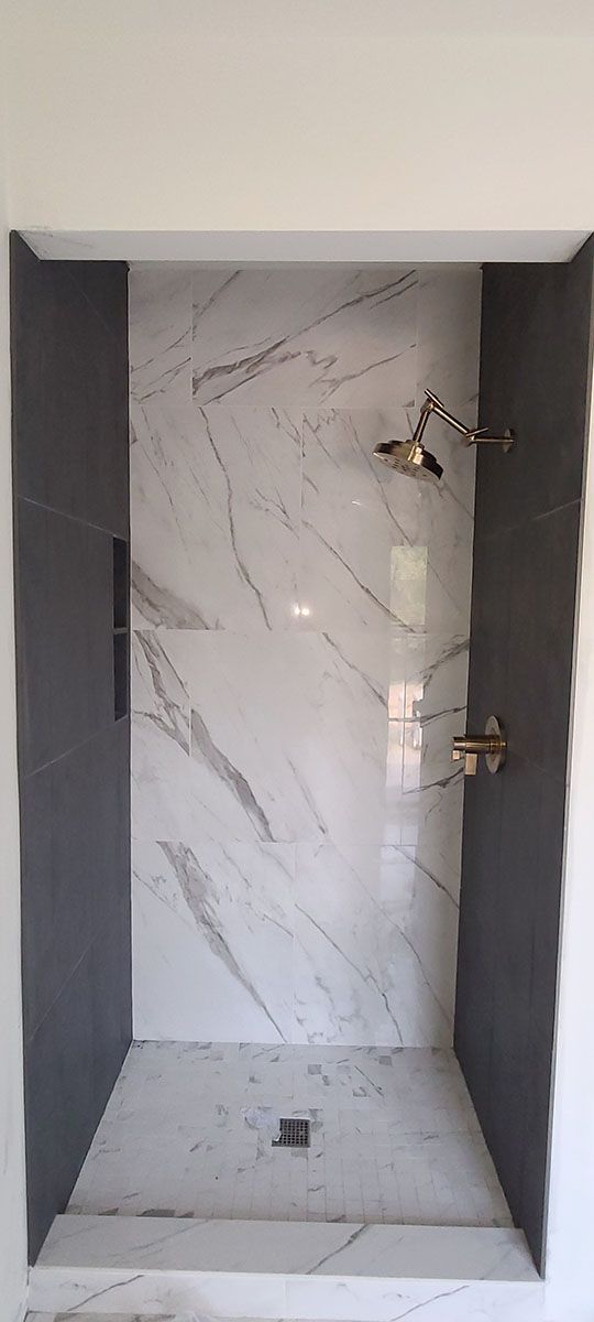 A walk-in shower with marble walls, dark gray side walls, and gold shower fixtures