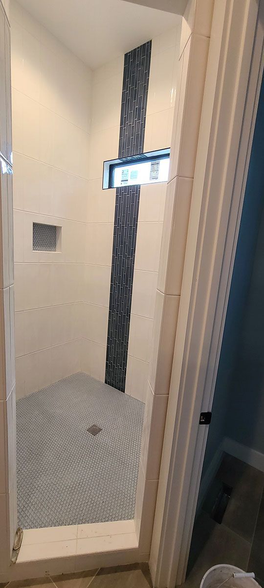 A newly renovated shower with light gray floor tiles and a dark blue accent