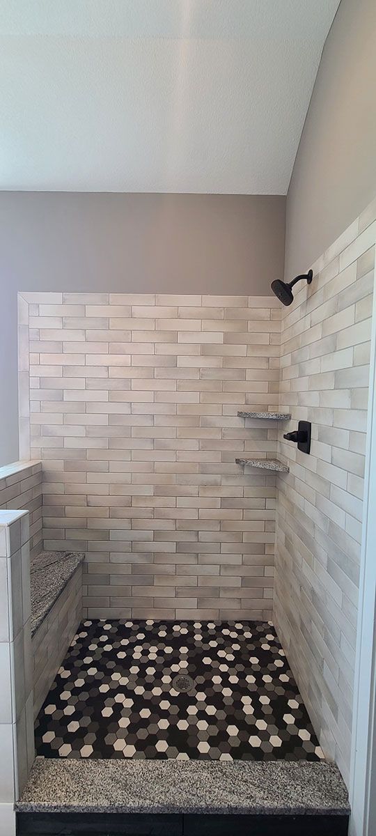 Walk-in shower with stone tile walls, pebble floor, and dark fixtures