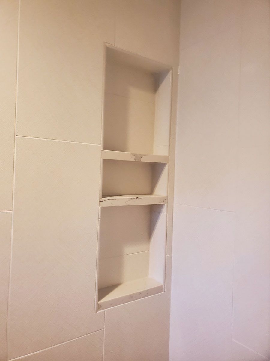 Built-in tiled shower niche with two shelves, recessed in a white tiled wall