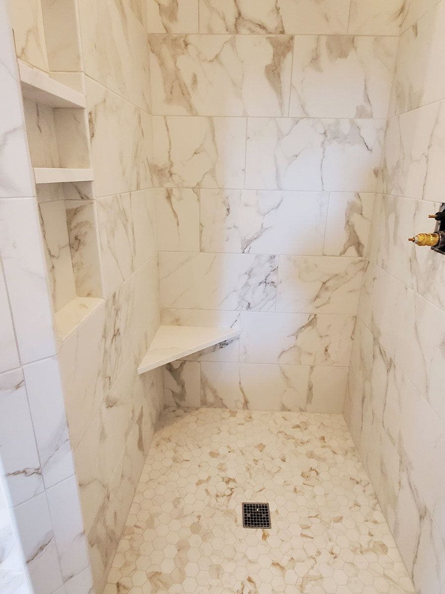 A newly tiled shower with white marble-patterned walls, a corner seat, and built-in shelves