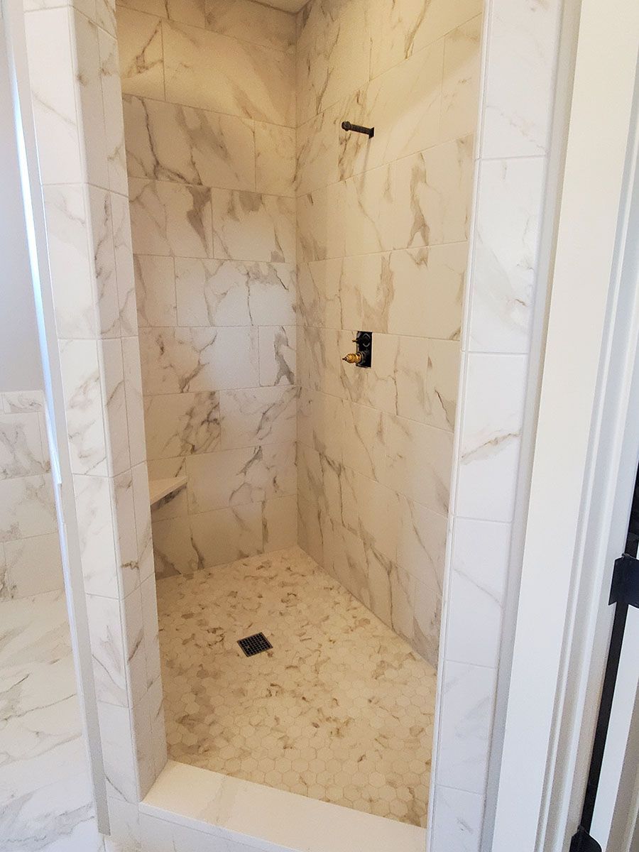 Marble-tiled walk-in shower with a seat and black shower fixtures