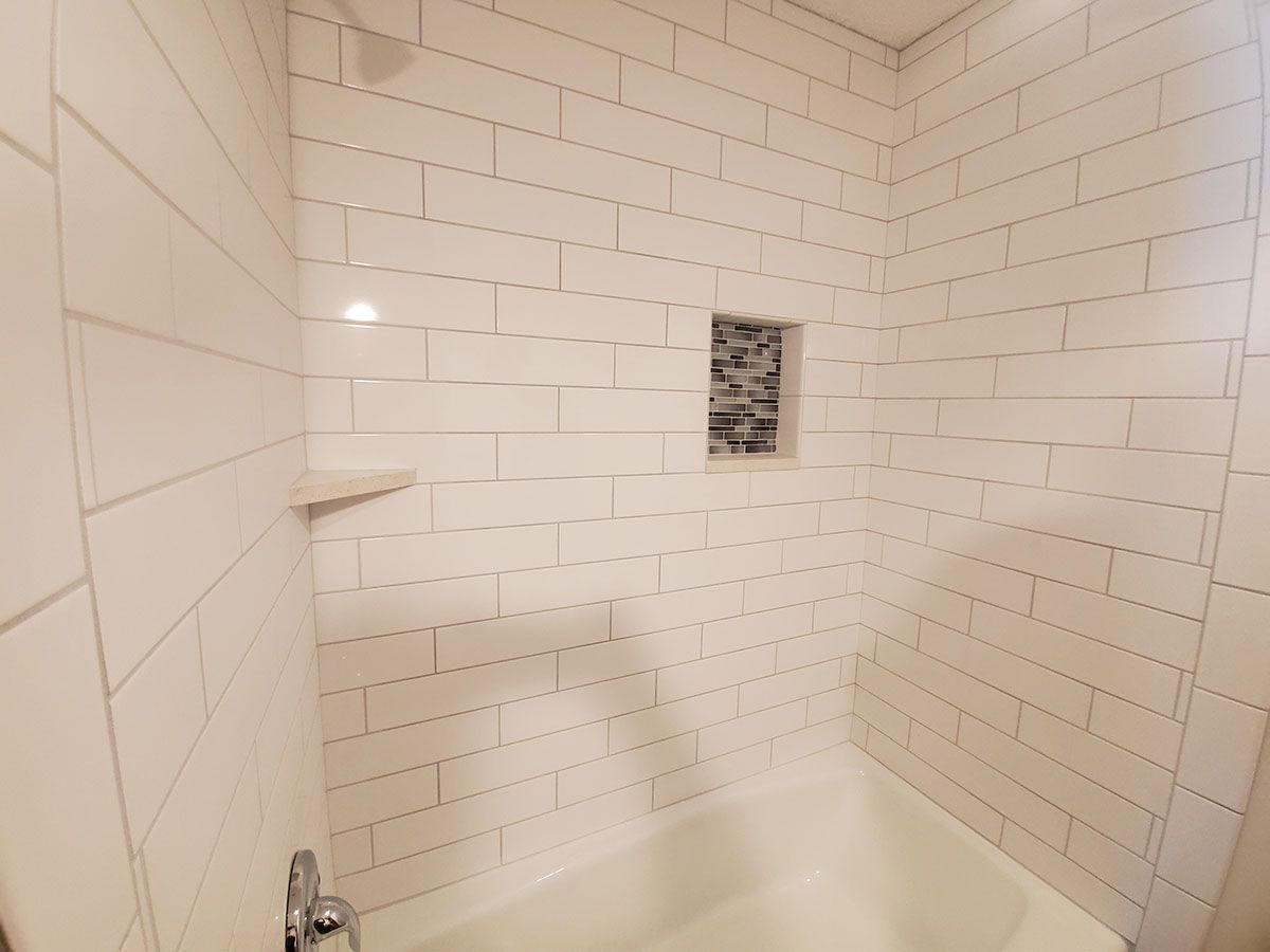 White tiled shower with a built-in shelf and niche, over a white bathtub