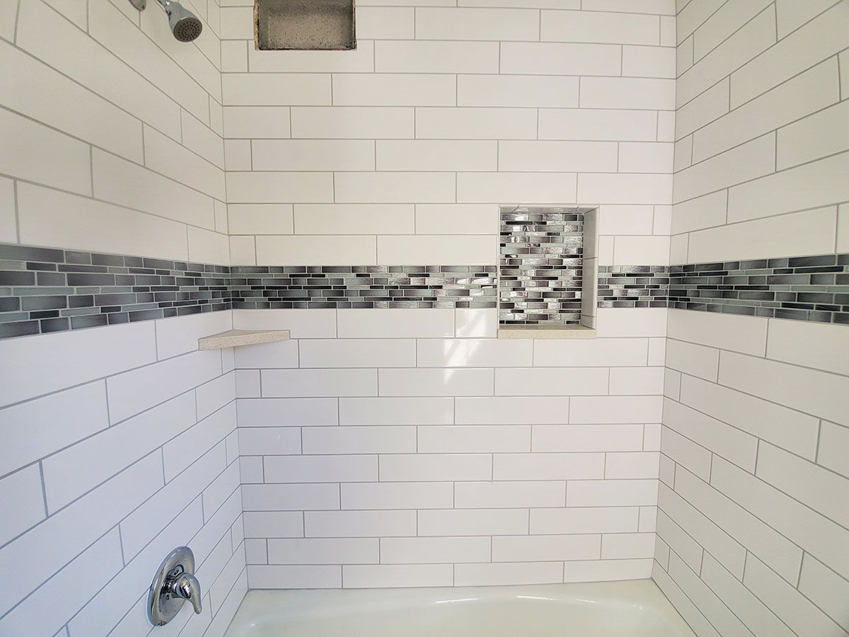White tiled shower with a gray mosaic accent and built-in shelf