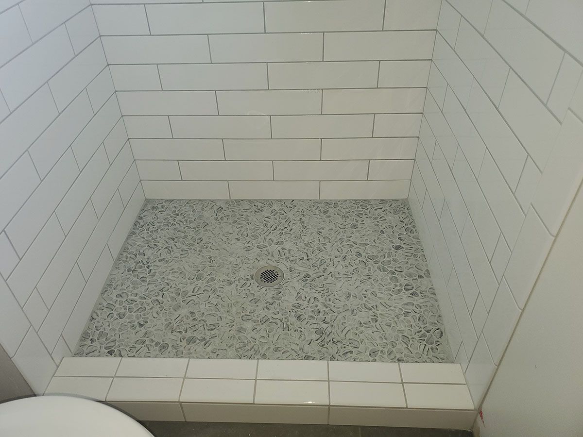 Shower stall with white rectangular wall tiles and a gray stone floor