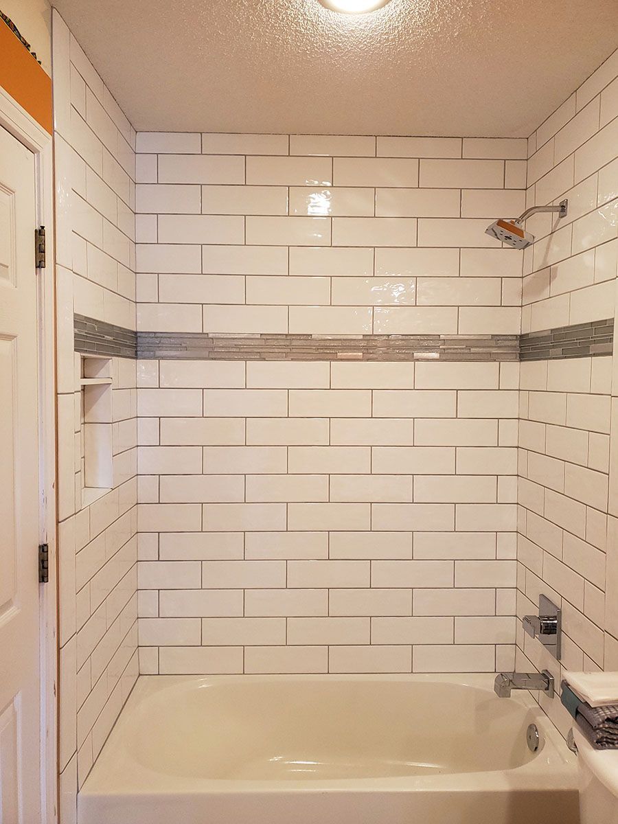 White-tiled shower with a decorative mosaic band and chrome fixtures over a bathtub