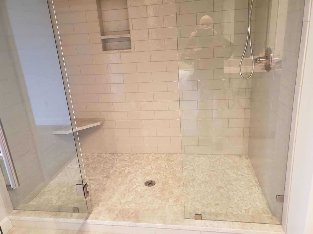 Glass-enclosed shower with white tiled walls, a stone floor, and a built-in shelf