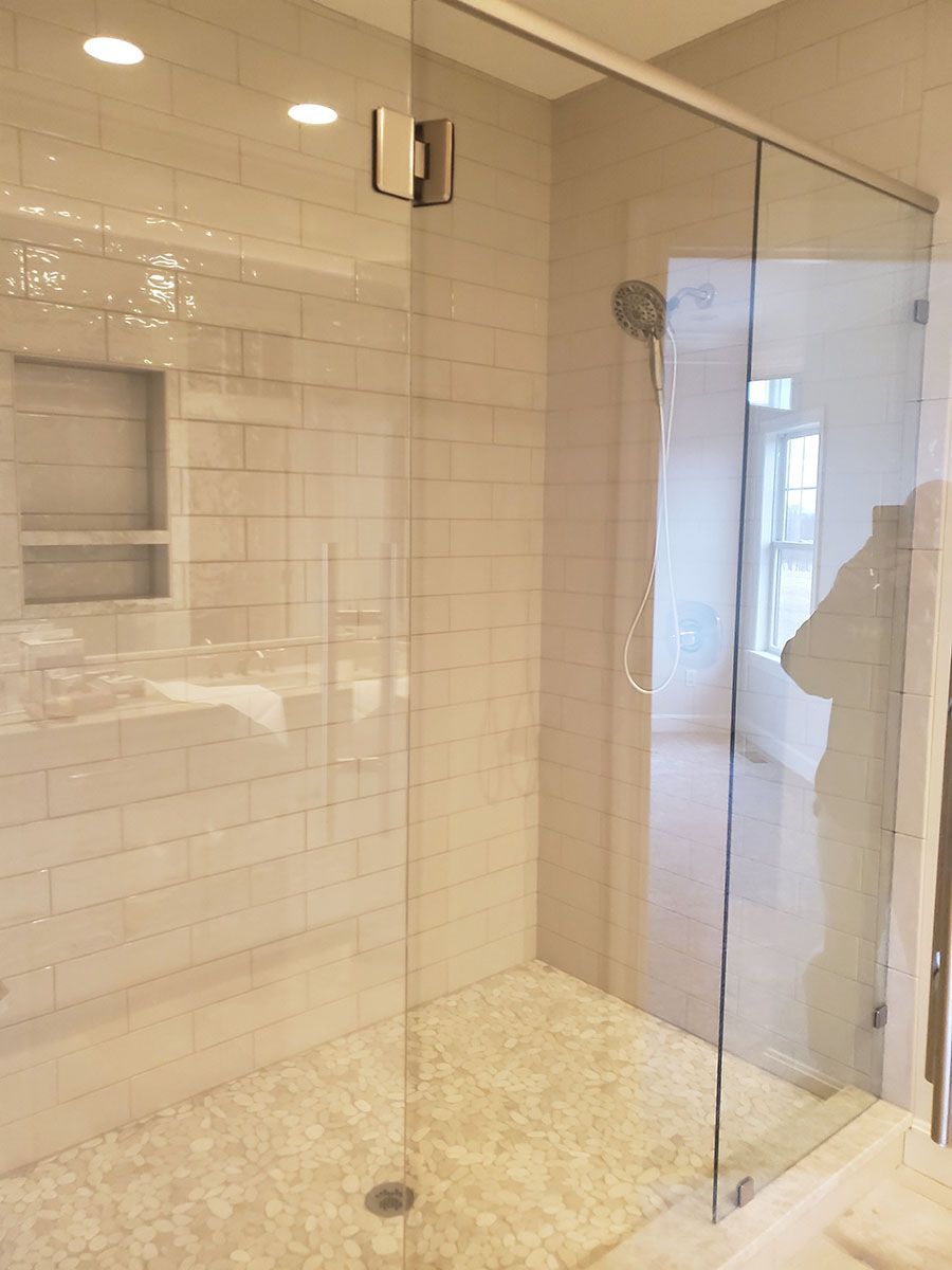 Glass shower with white tile walls and pebbled floor