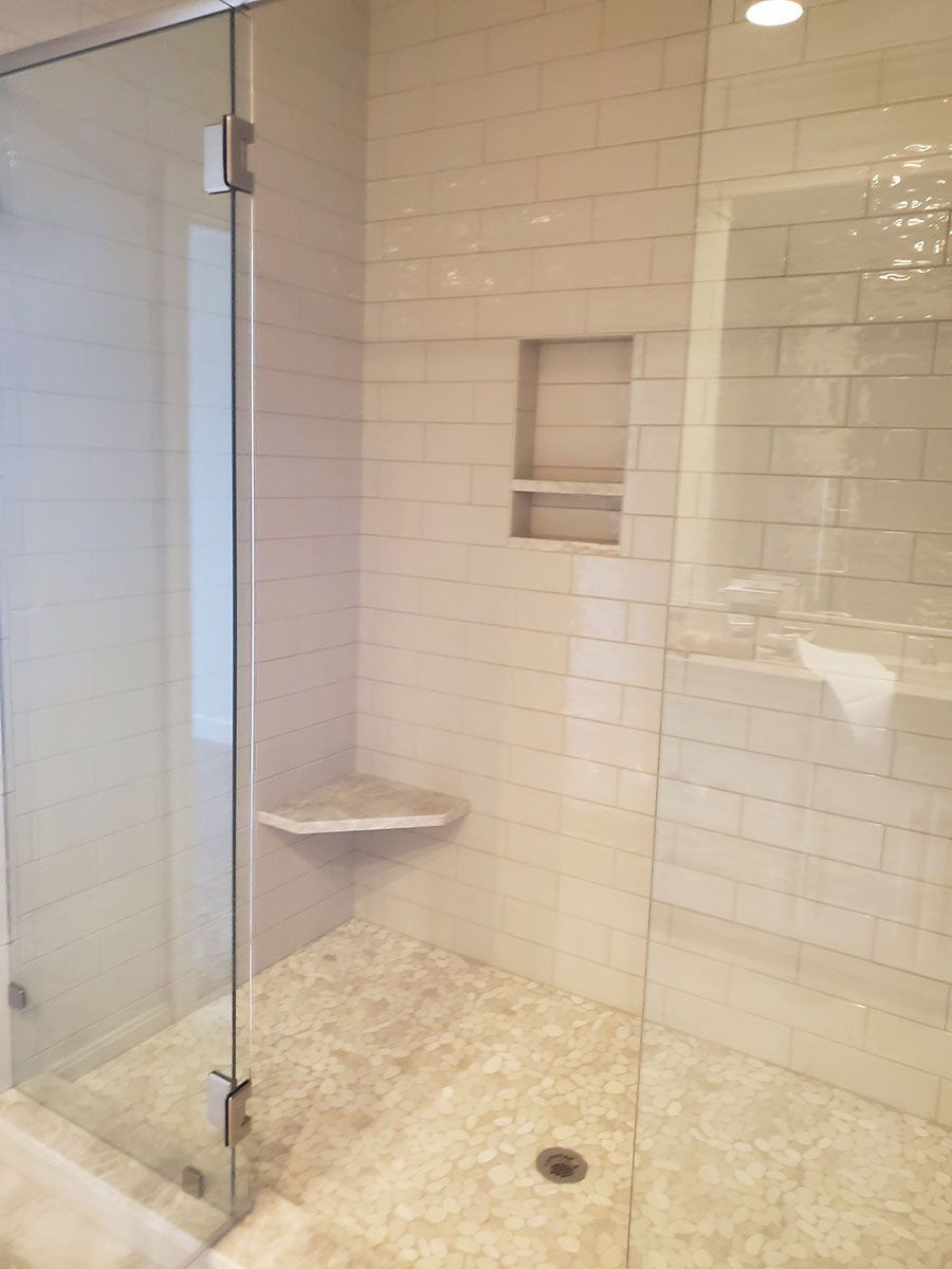Glass-enclosed shower with white subway tile walls, a built-in corner seat, and a recessed shelf
