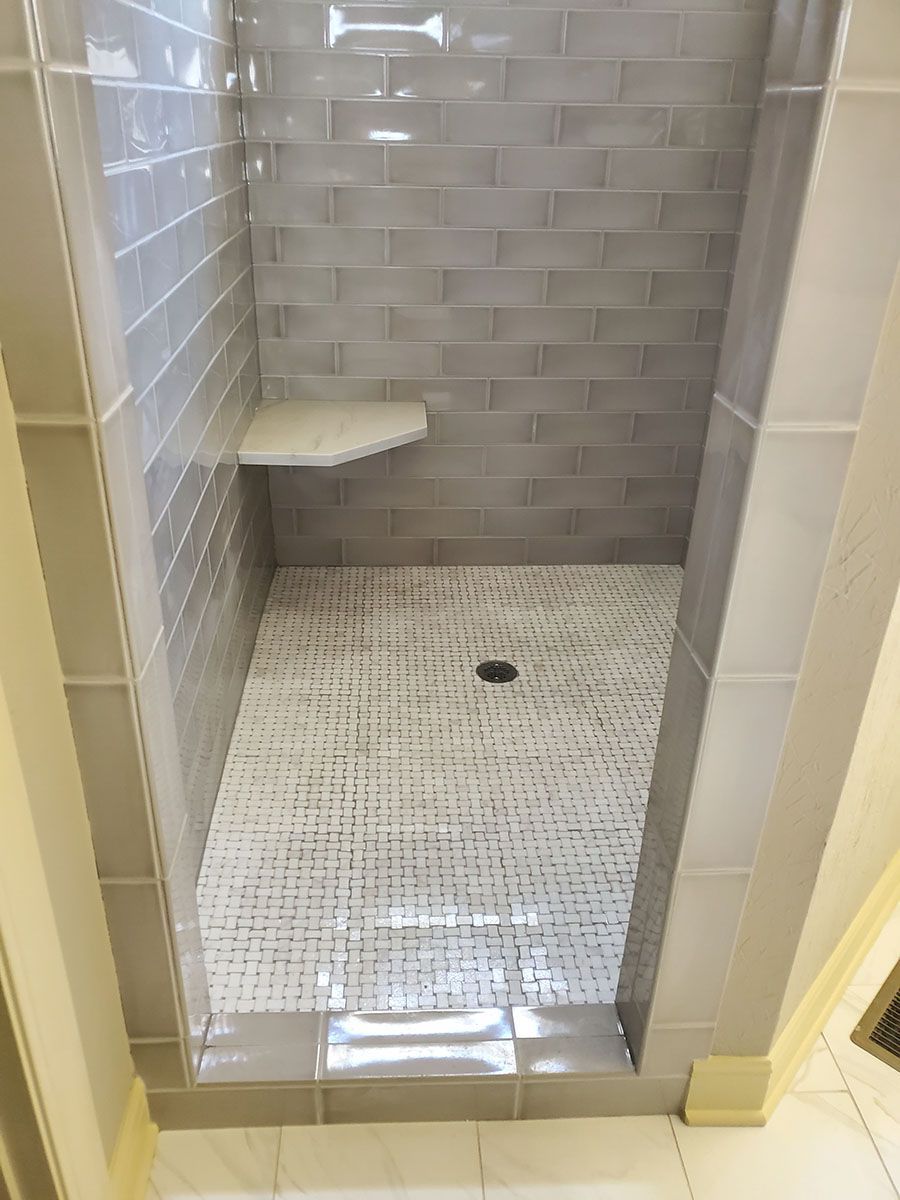 Tiled walk-in shower with gray subway tiles, small white floor tiles, and a built-in seat