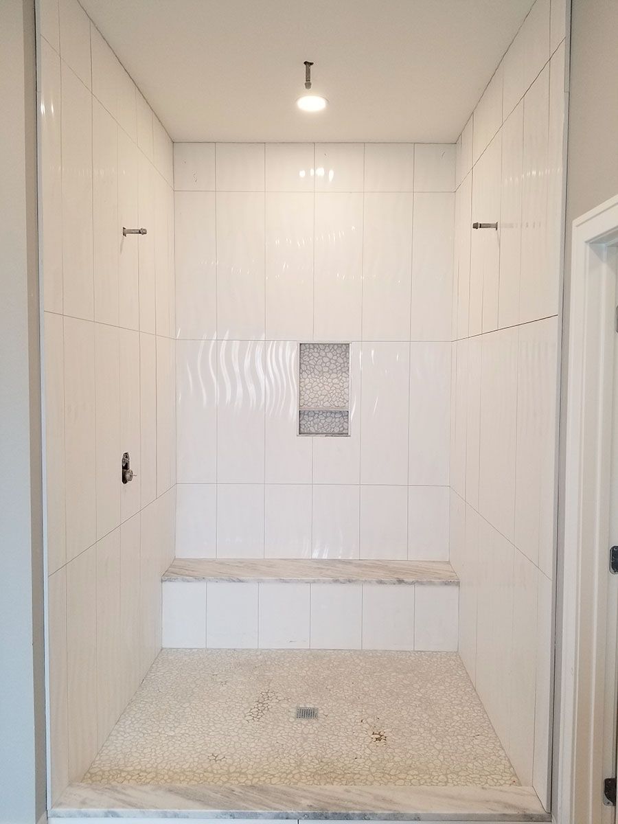 White tiled shower with pebble floor, built-in bench, and recessed shelf