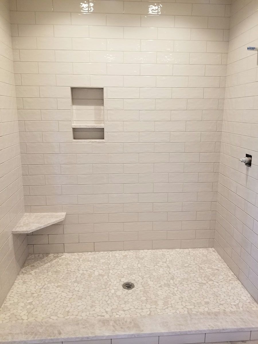 Shower with light-colored stacked tile walls, pebble tile floor, built-in shelf and bench