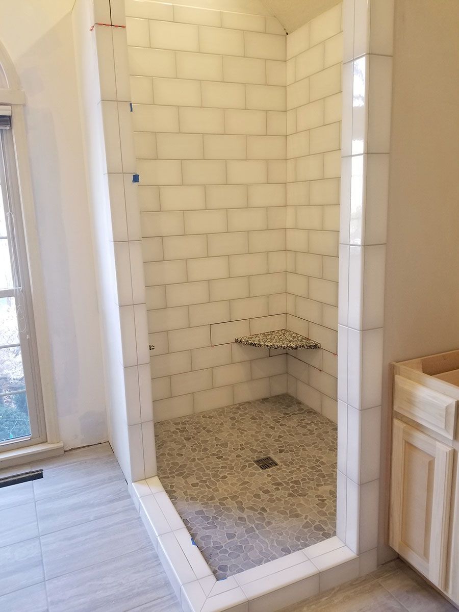 Completed tiled shower with pebble floor, built-in seat, and white subway tile walls