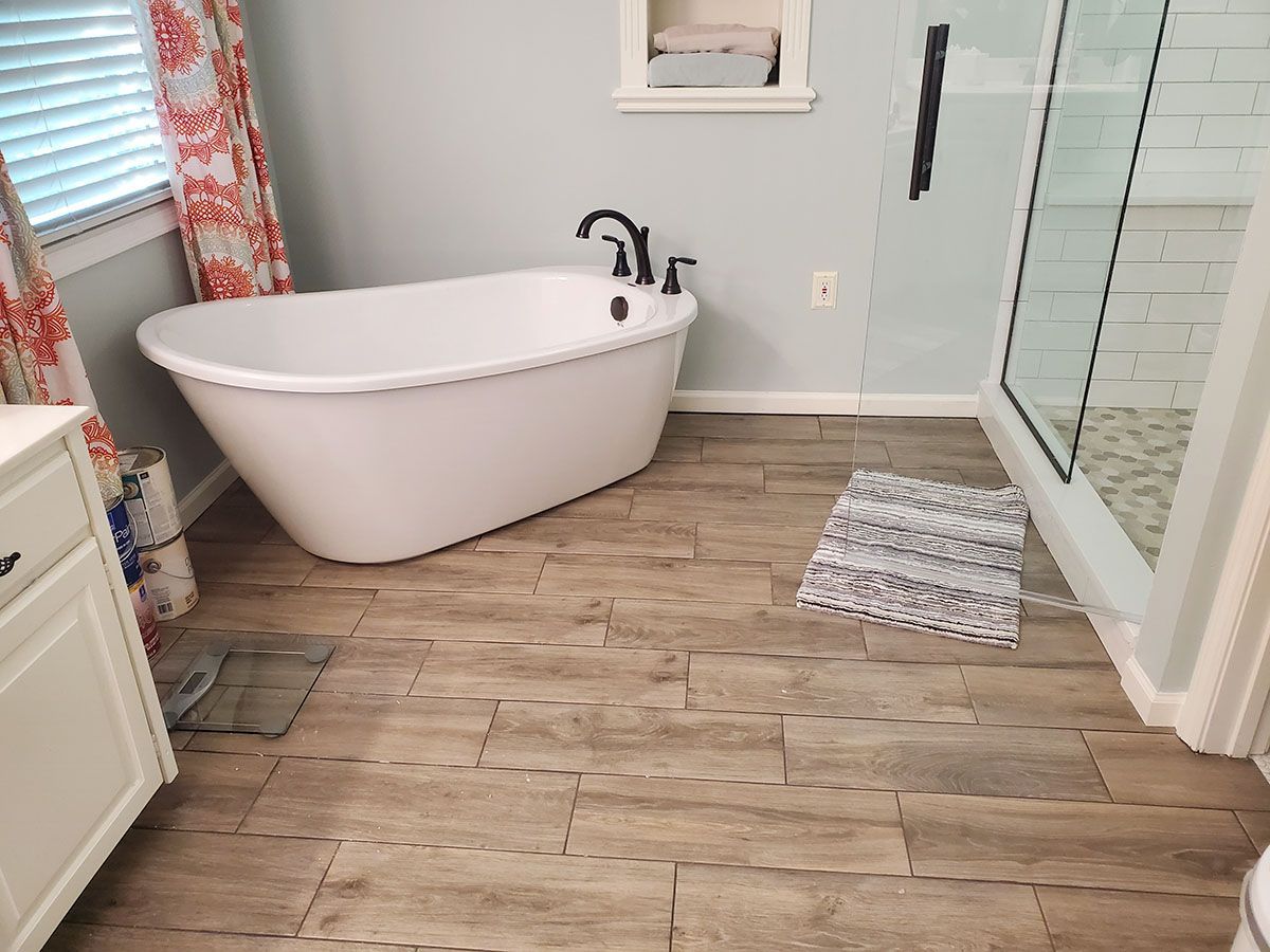 Bathroom with a white freestanding tub, wood-look floor tiles, and a glass shower enclosure