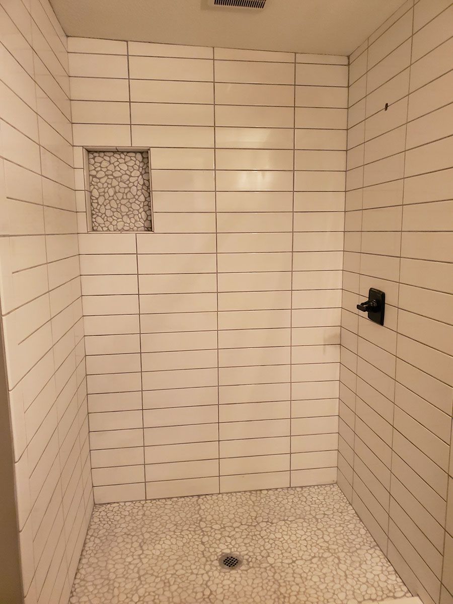 Shower with white textured tile walls, pebble floor, and a built-in shelf