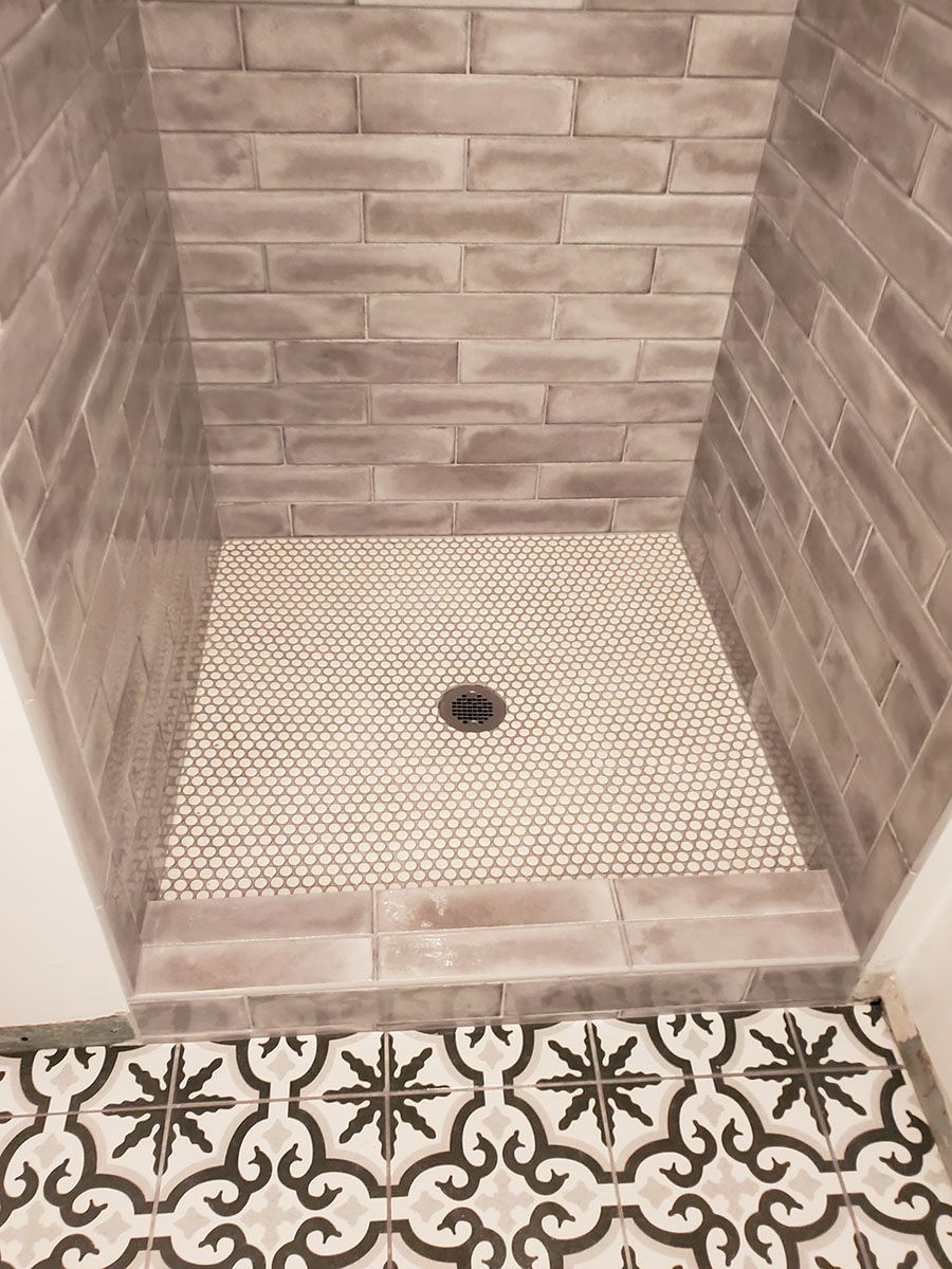 Shower stall with gray brick-style tile walls and small round mosaic tile floor