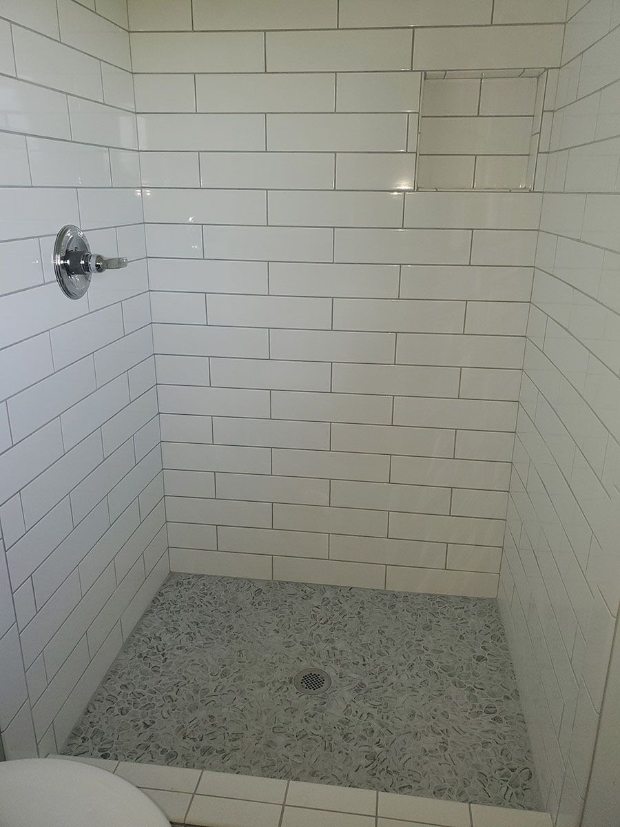White tiled shower with a pebble-stone floor and a chrome showerhead