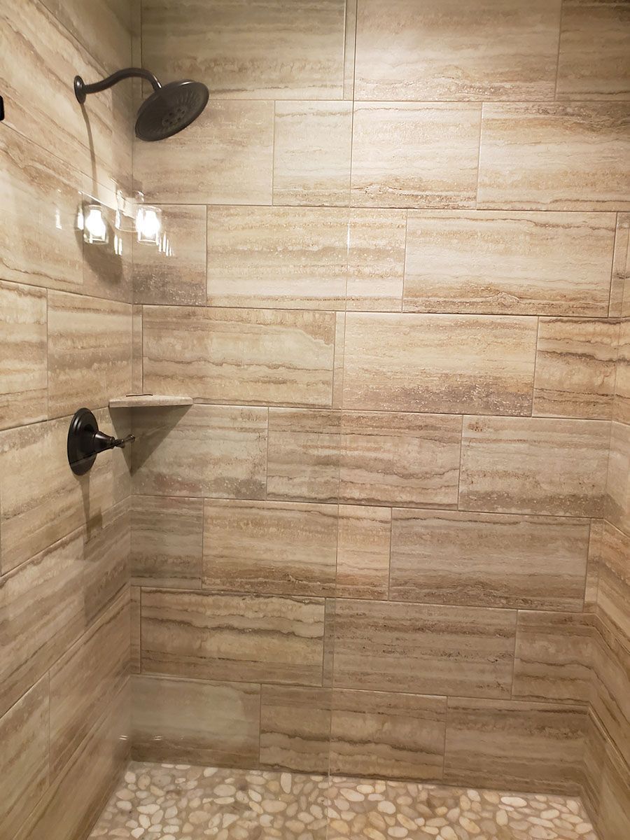 Shower with tan-colored, horizontal tiled walls, a pebble floor, and black fixtures