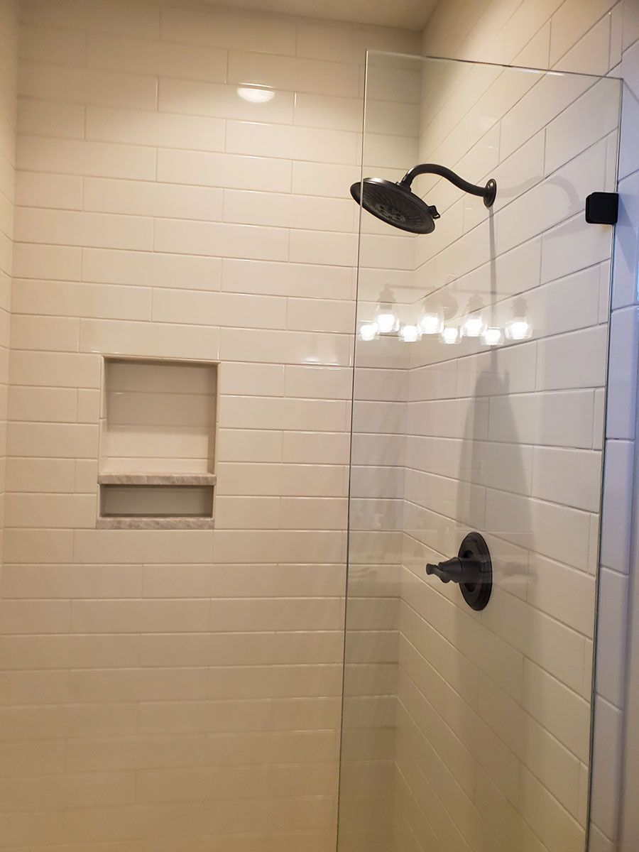 Shower stall with glass door, black fixtures, and white tiled walls