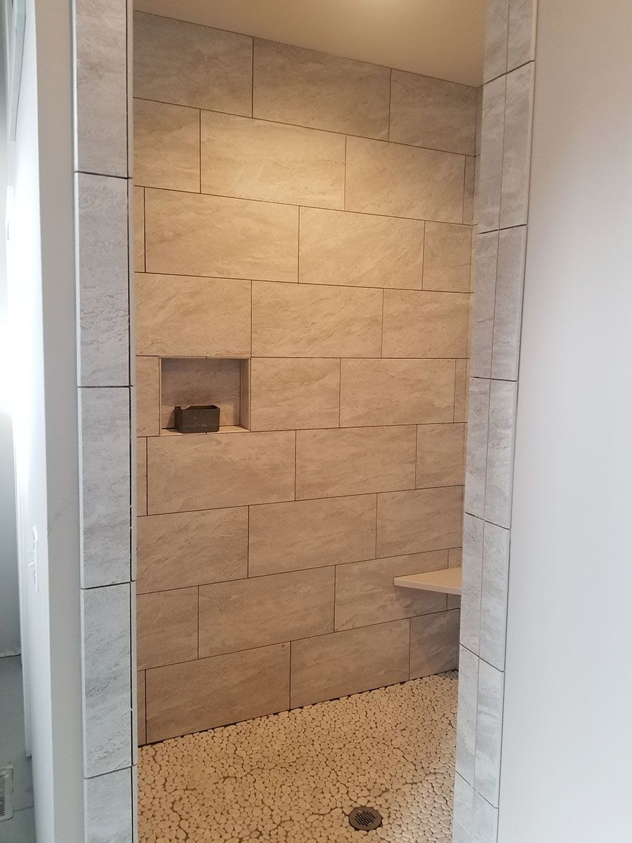 Tiled shower with pebble floor, built-in bench, and a small recessed shelf
