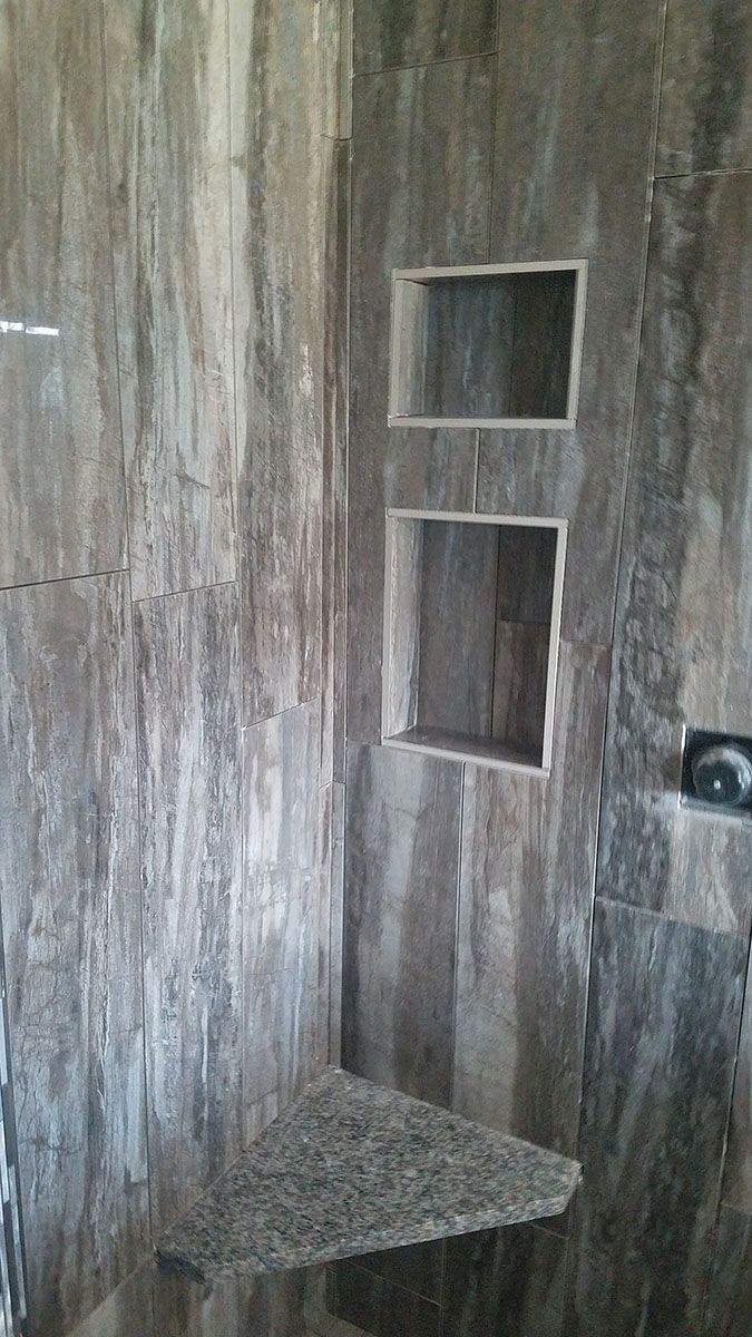 Shower interior with gray marbled tile, two built-in shelves, and a corner shelf