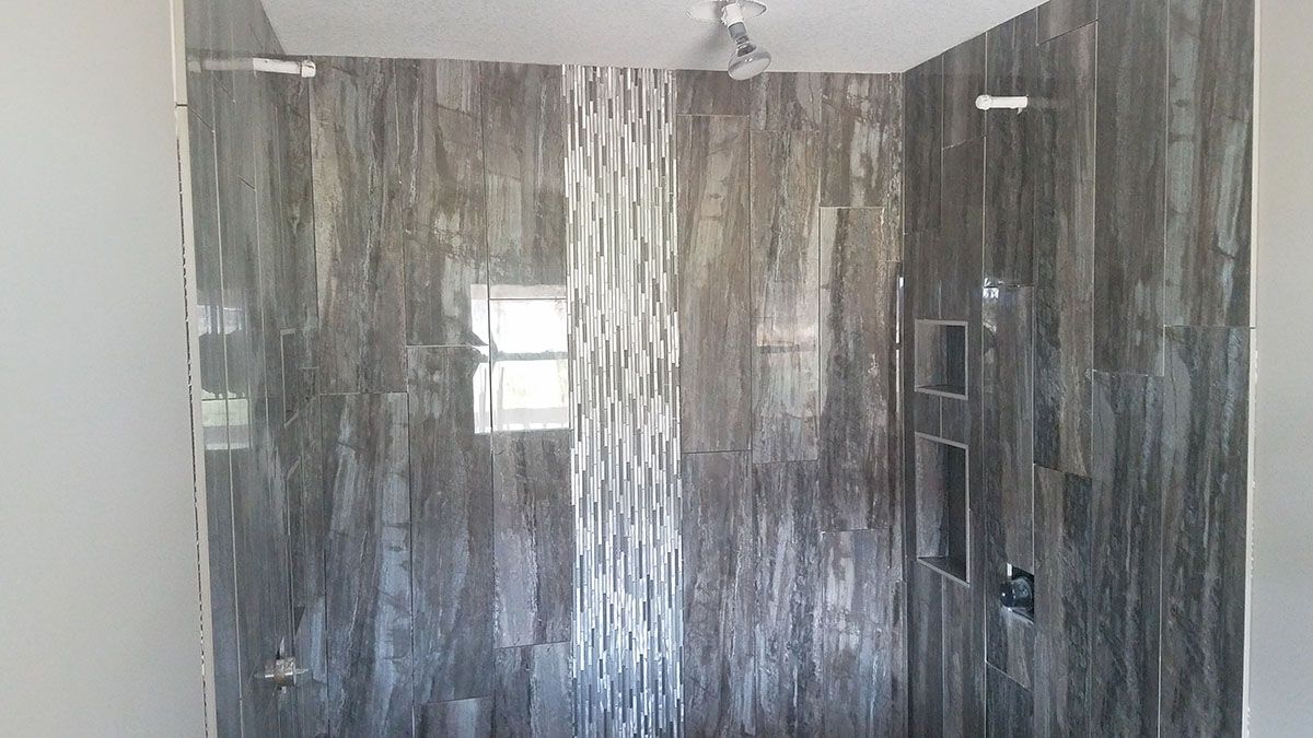 Shower with dark gray and textured tile walls, glass door, and recessed shelves