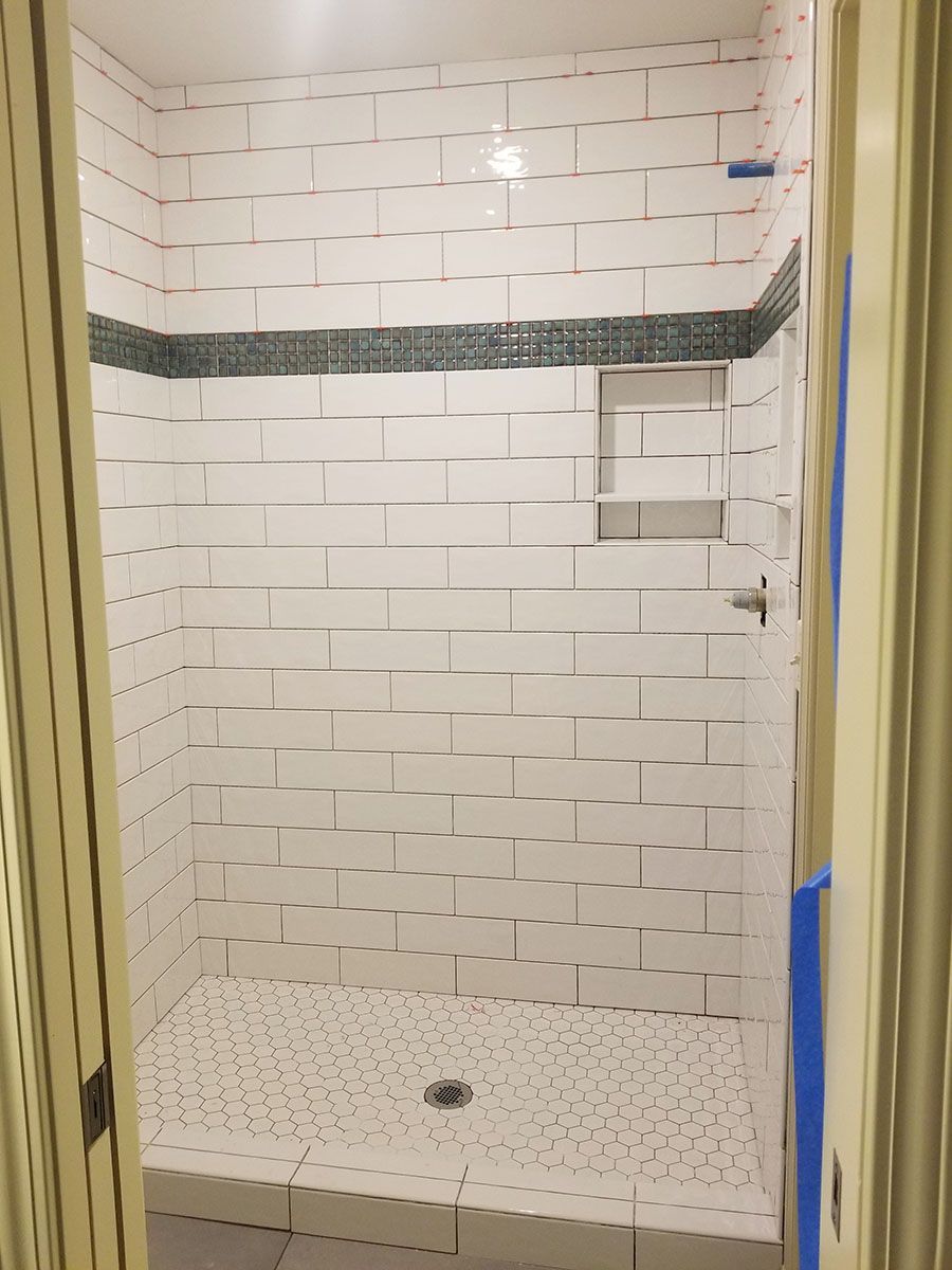 White tiled shower with gray floor, a dark decorative tile strip, and built-in shelves