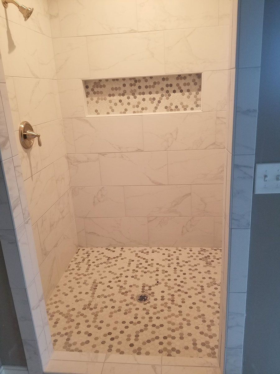 Tiled shower with a built-in shelf. White walls with a mosaic-tiled floor and shelf