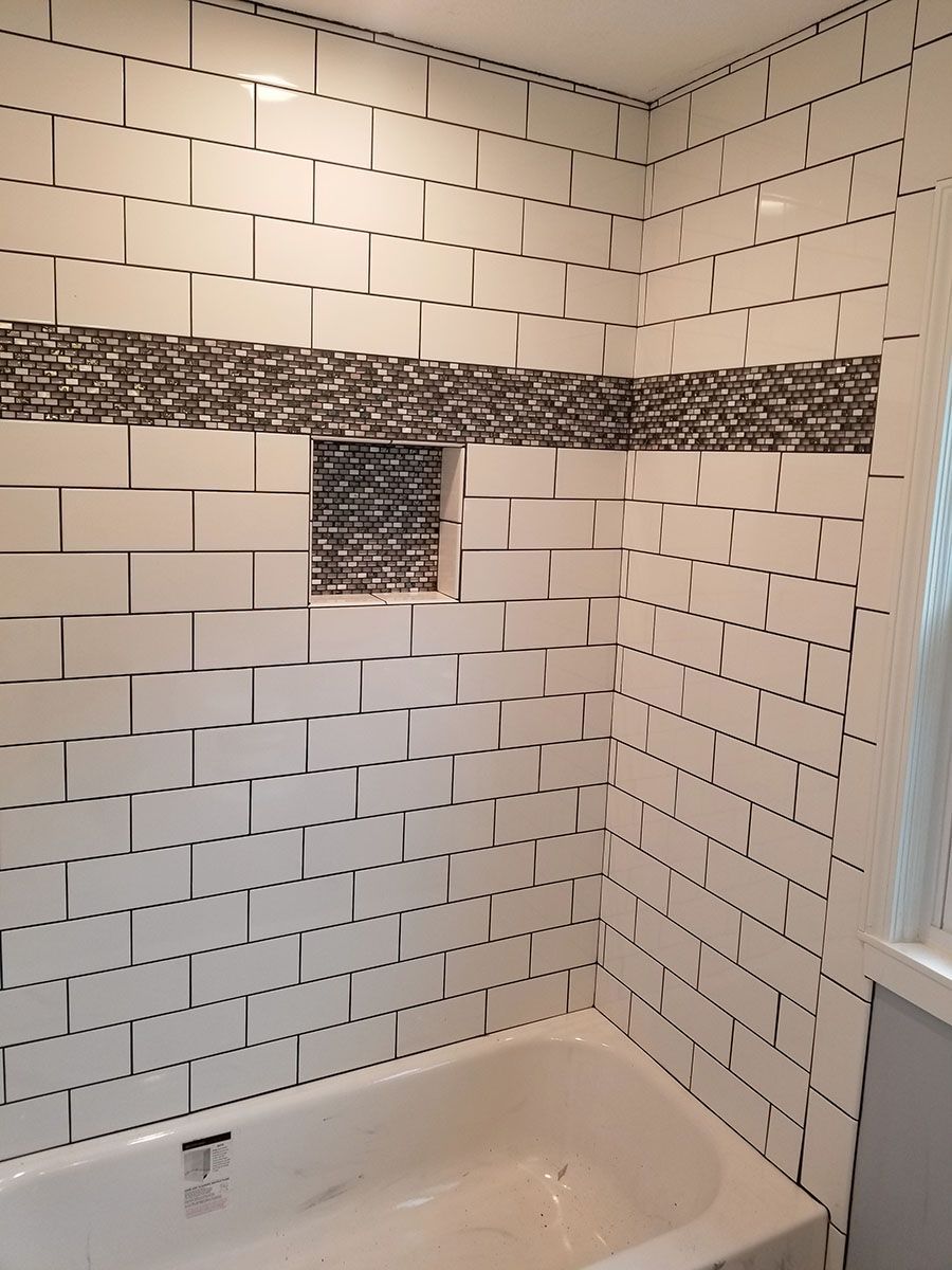 Tiled bathroom shower stall with white subway tiles and a decorative dark mosaic band