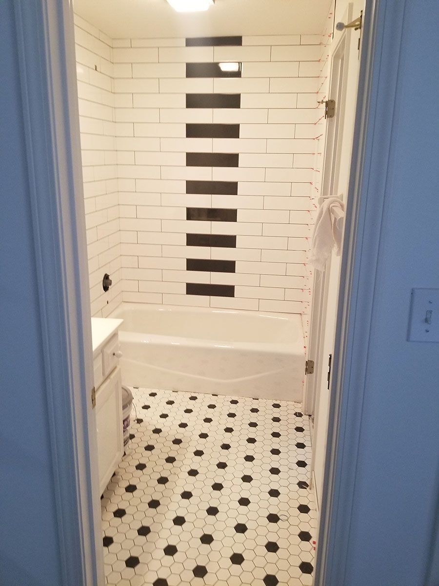 Bathroom with white and black tiled walls and floor, tub, and vanity