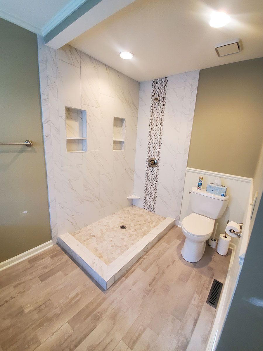A modern bathroom with a tiled shower, toilet, and light-colored wood-look flooring