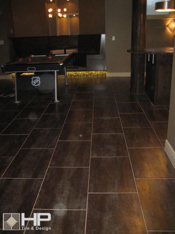 Dark brown tile flooring in a basement recreation room, with a pool table and bar area visible