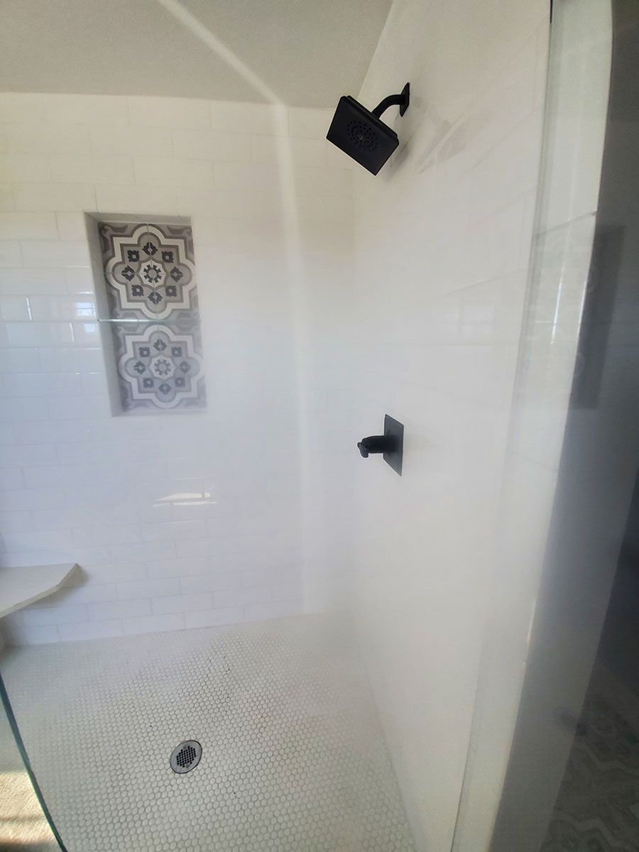 White tiled shower with black fixtures; decorative niche with mosaic tile