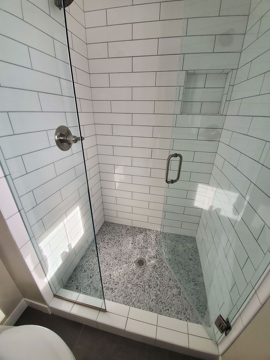 Tiled shower with glass doors, silver fixtures, and pebble tile floor