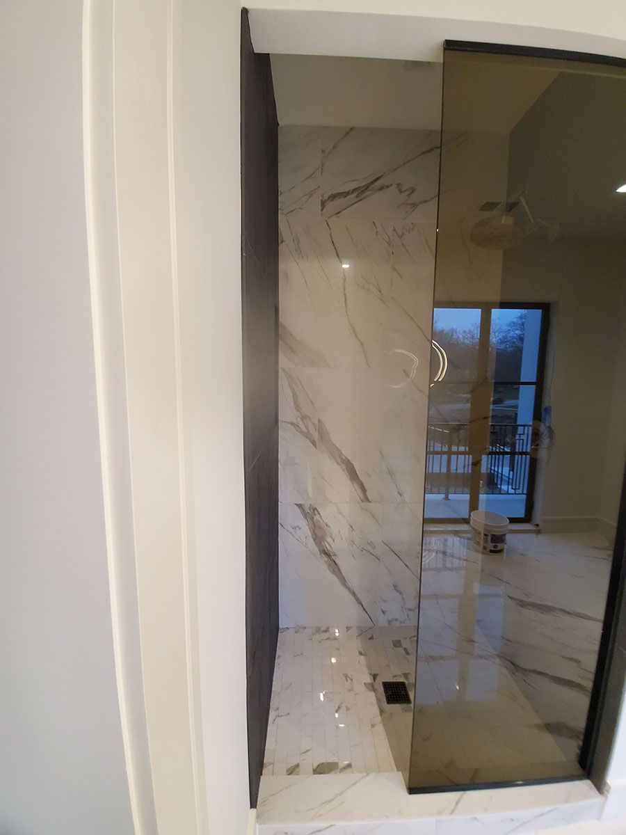 Marble-tiled shower with glass door and black drain