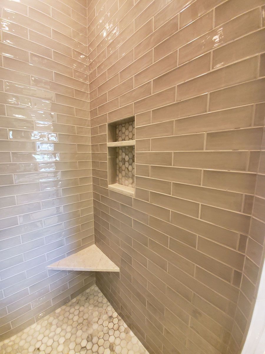 Shower with gray rectangular tiles, a corner seat, and a built-in shelf with decorative tile