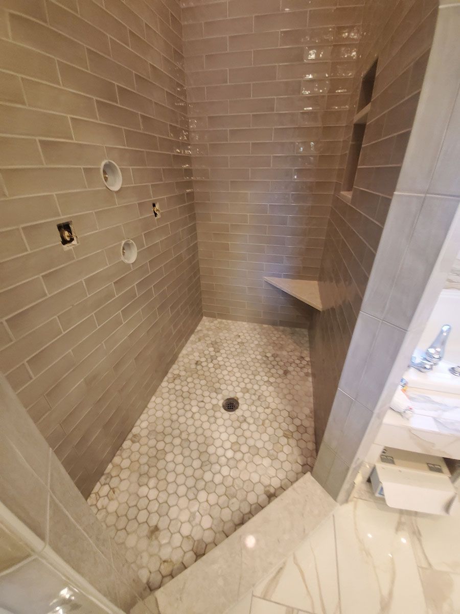 Tiled shower with gray brick-like walls, mosaic floor, built-in seat, and open shelves; light fixtures visible