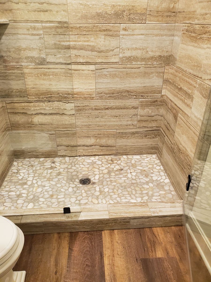 Shower stall with brown stone wall tiles and pebble floor